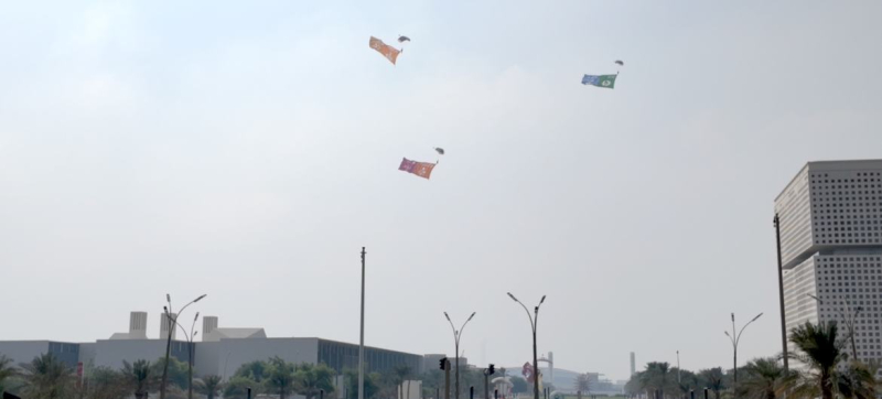 Катарская парашютно-десантная команда выполняет воздушное шоу, снижаясь над QNCC, неся 17 красочных флагов Целей устойчивого развития, а также флаги ООН и Катара.