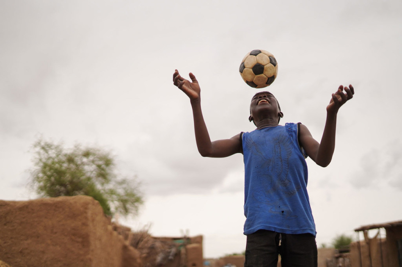 Десятилетний мальчик играет в футбол в лагере для внутренне перемещенных лиц в Абушоке, Судан.